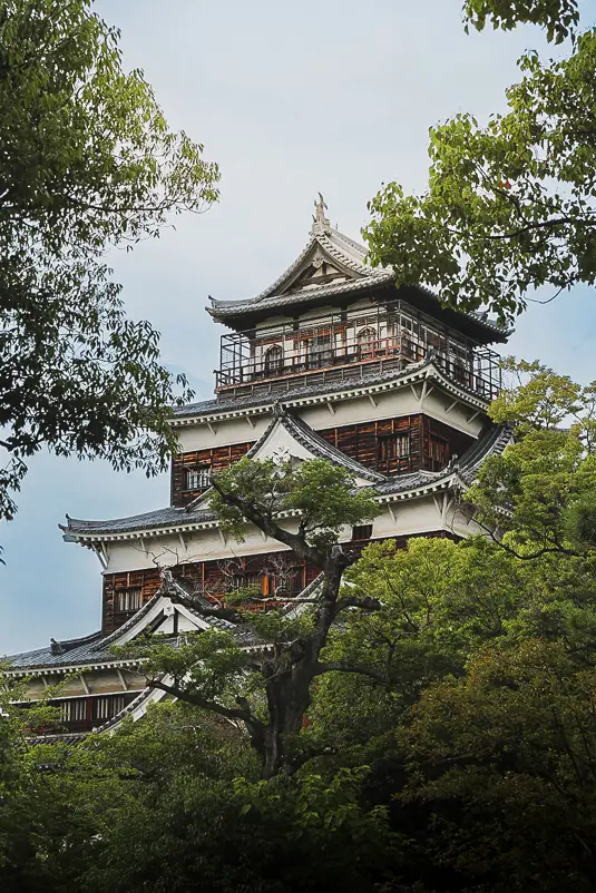 Het hoofdgebouw van Hiroshima Castle, geframed door groene bomen