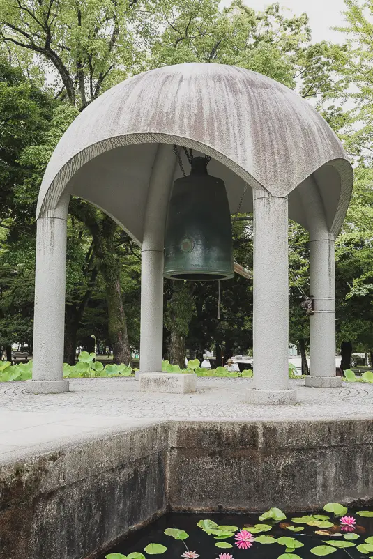De Peace Bell in het Hiroshima Peace Memorial Park, omringd door groen en waterlelies