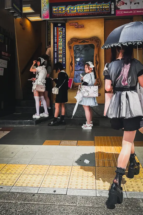 Maid café-medewerkers en bezoekers in cosplay voor de ingang van een themawinkel in Denden Town, Osaka.