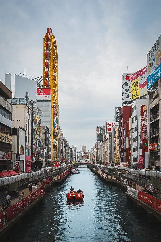 Zicht op het Dotonbori-kanaal in Osaka met het gele reuzenrad van Don Quijote en een bootje op het water.