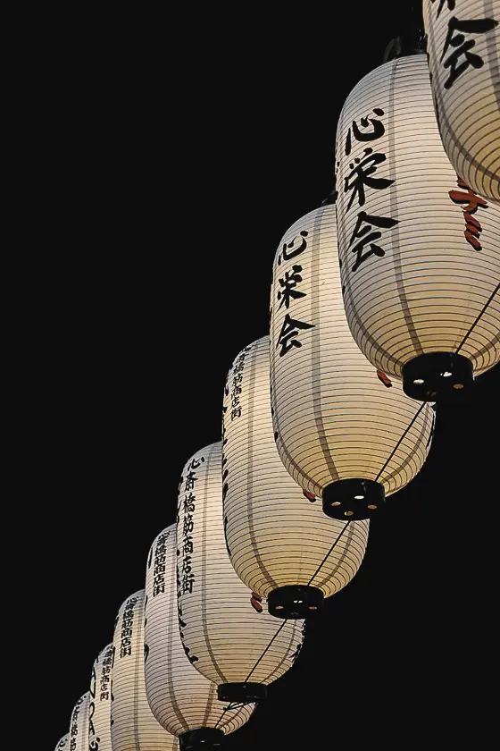 Rij van traditionele Japanse papieren lantaarns tegen een donkere avondlucht.