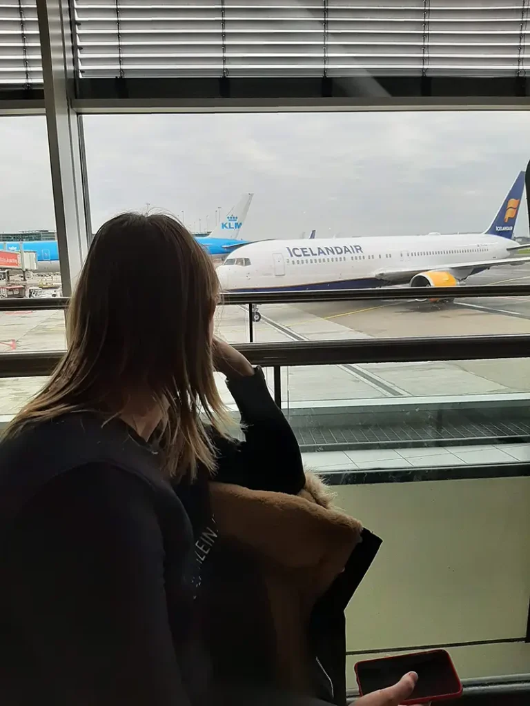 Reiziger wacht aan de gate op een vlucht terwijl vliegtuigen op de achtergrond staan om goedkope vluchten te nemen