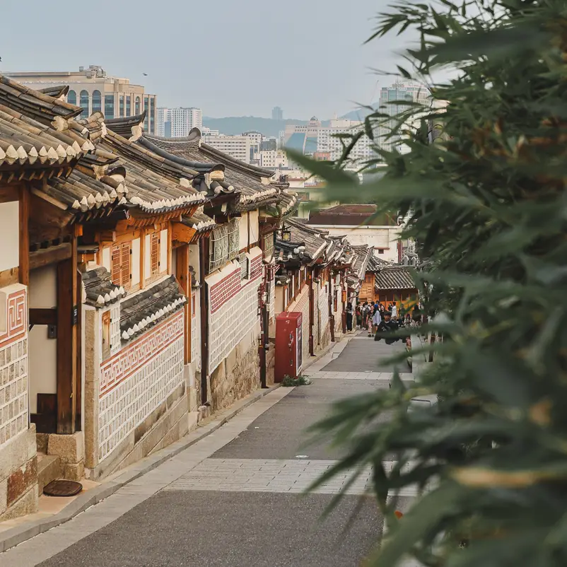 Uitzicht over een straat met traditionele hanokhuizen in Bukchon Hanok Village met de skyline van Seoul op de achtergrond