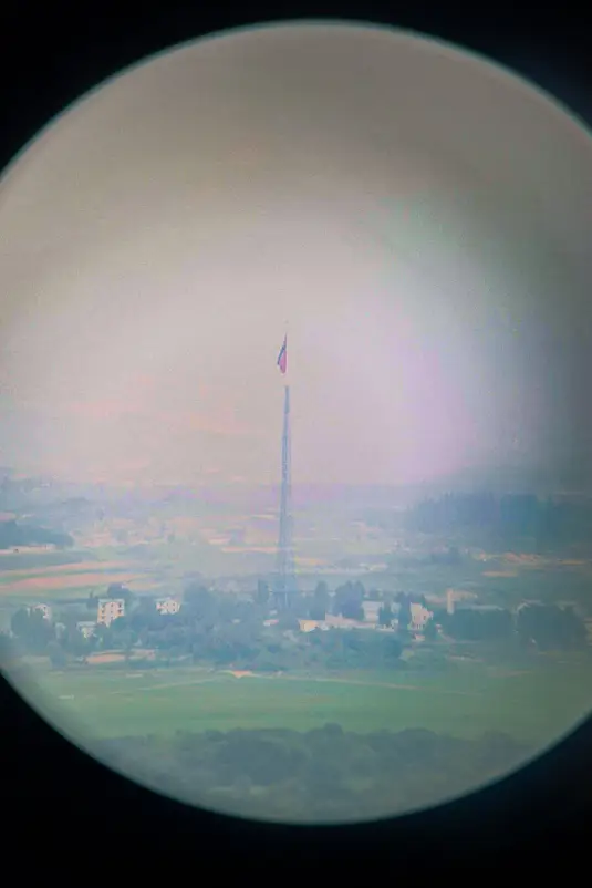 Uitzicht op een Noord-Koreaans dorp met vlag gezien door de telescoop op Dora Observatory tijdens de DMZ-tour